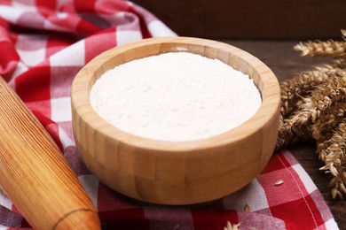 Photo of Flour in bowl and ears of wheat on wooden table, closeup