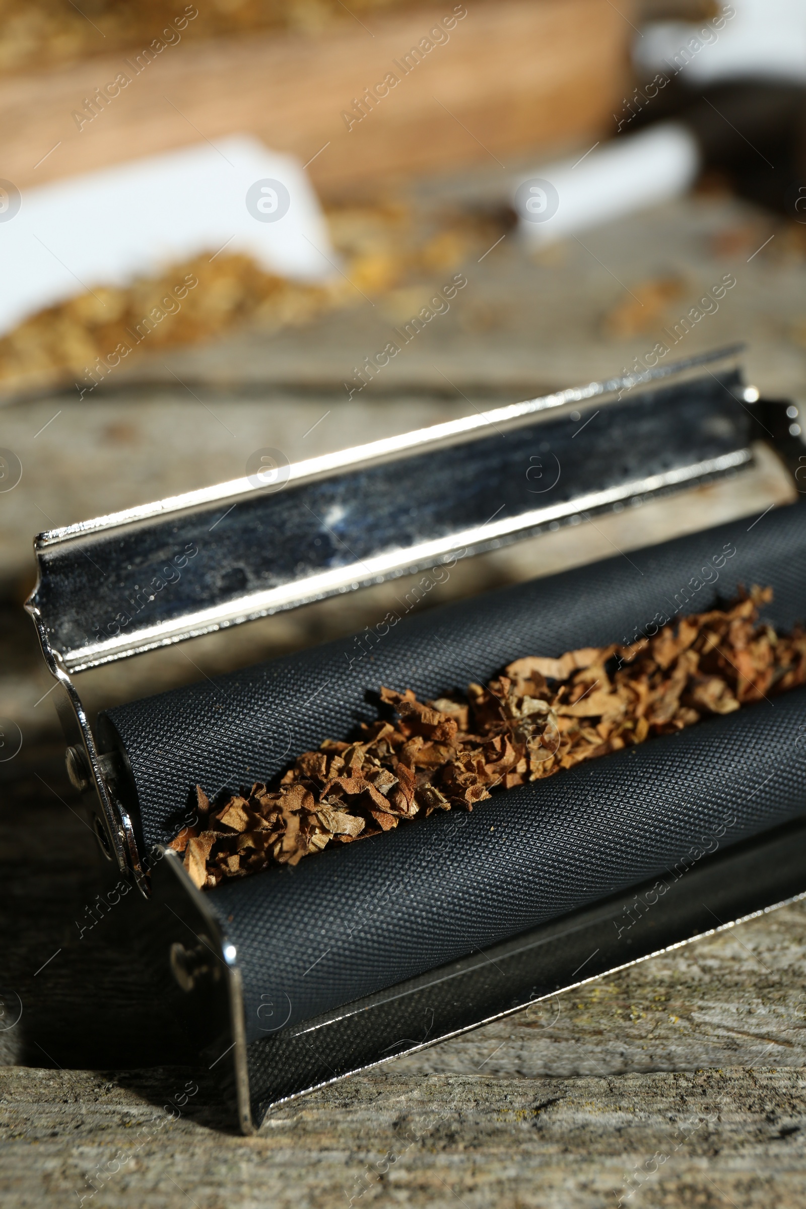 Photo of Roller with tobacco on old wooden table, closeup. Making hand rolled cigarettes
