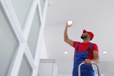 Photo of Electrician repairing ceiling lamp indoors, low angle view. Space for text
