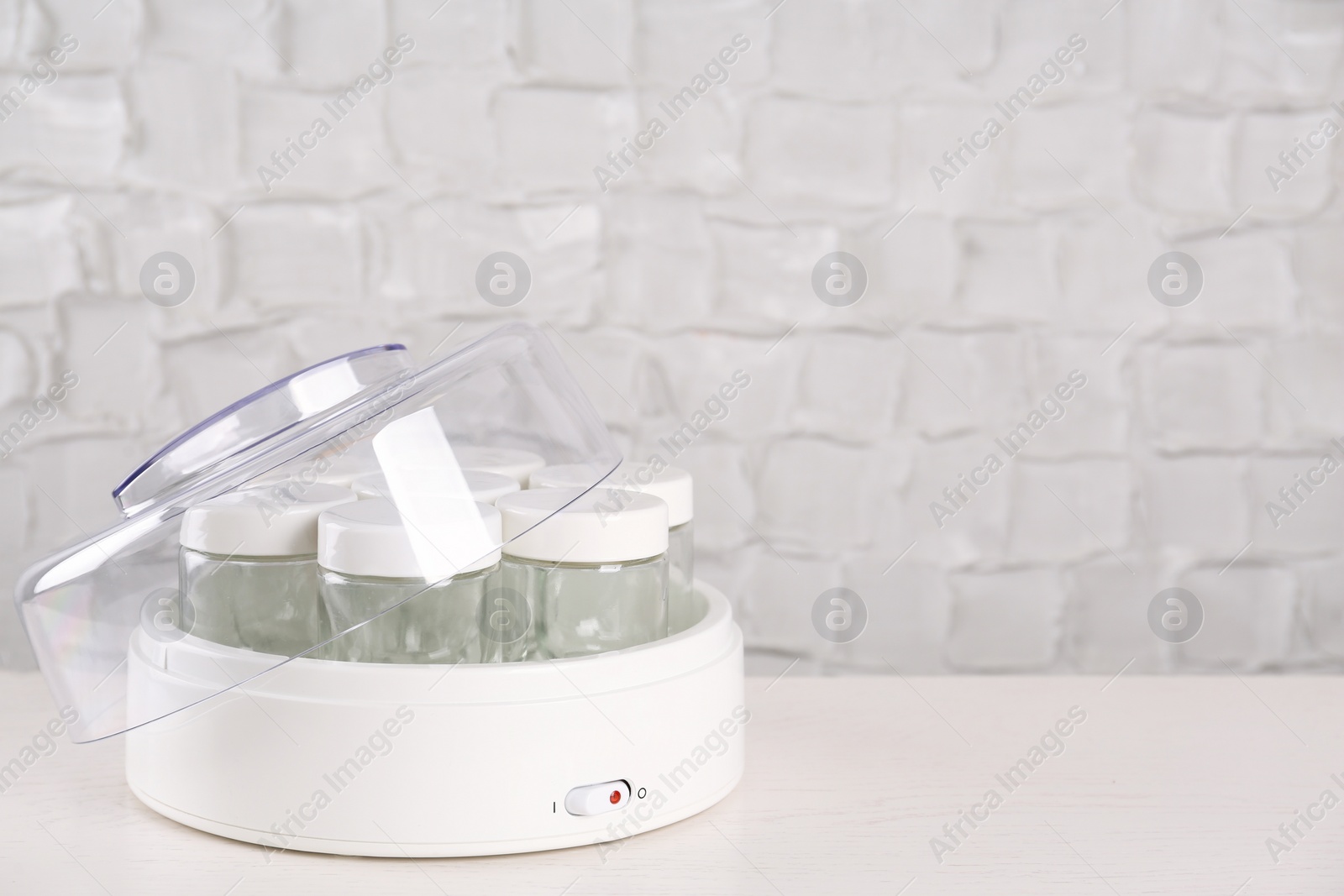 Photo of Modern yogurt maker with empty jars on white wooden table, space for text