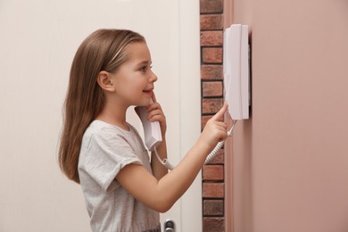 Photo of Cute little girl answering intercom call indoors