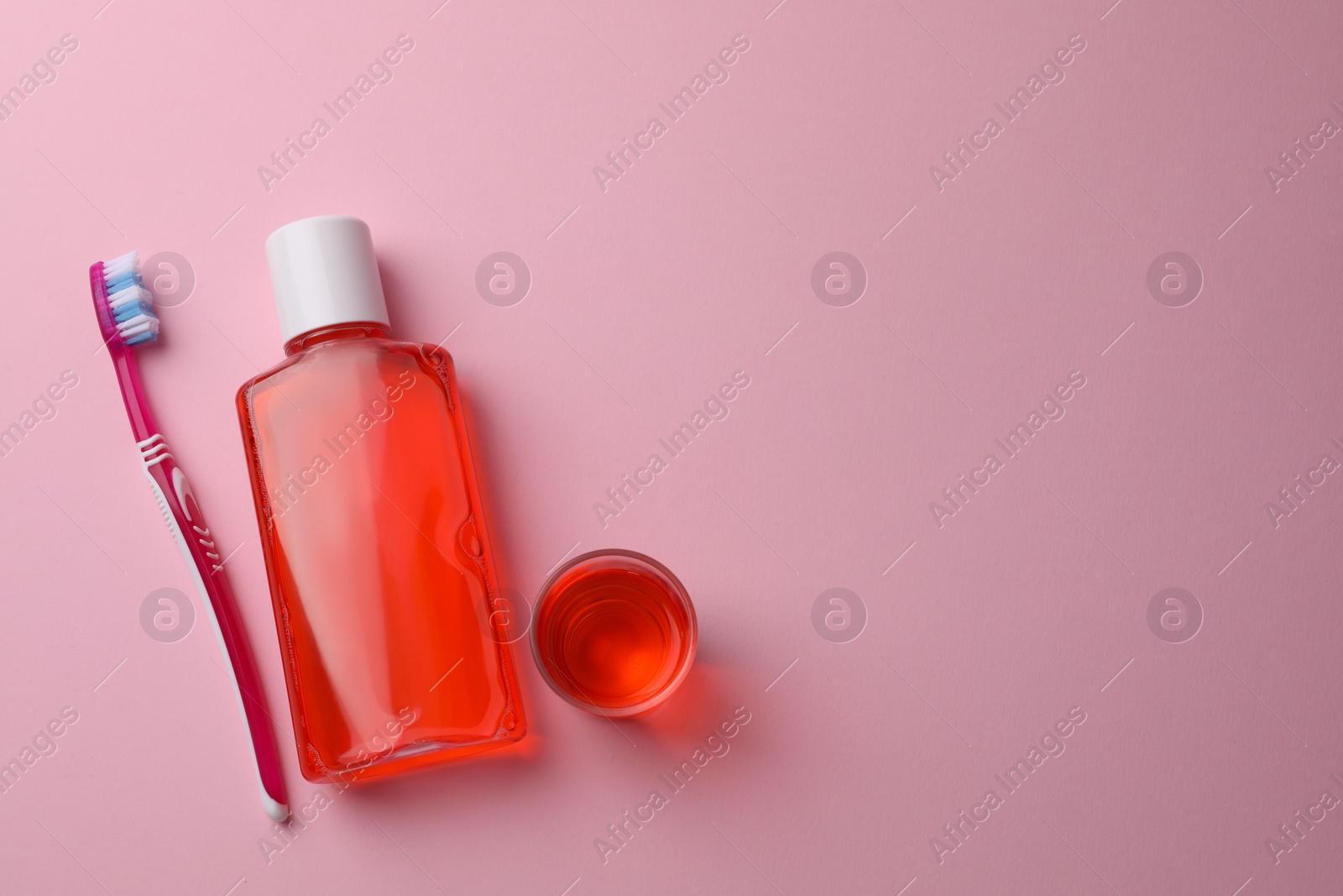Photo of Fresh mouthwash in bottle, glass and toothbrush on pink background, flat lay. Space for text