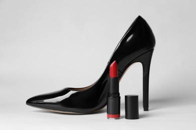 Photo of Beautiful red lipstick and black high heeled shoe on white background