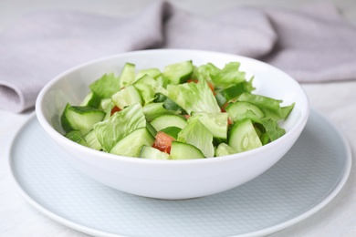 Bowl of vegetarian salad with cucumber, tomato and lettuce on table