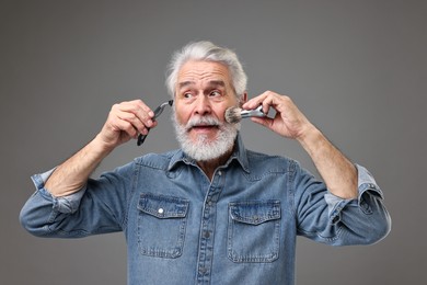 Photo of Senior man with mustache holding razor and brush on grey background
