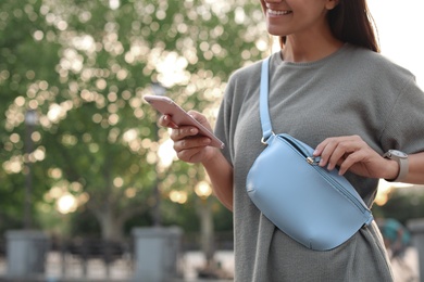 Photo of Young woman with stylish bum bag and smartphone outdoors, closeup