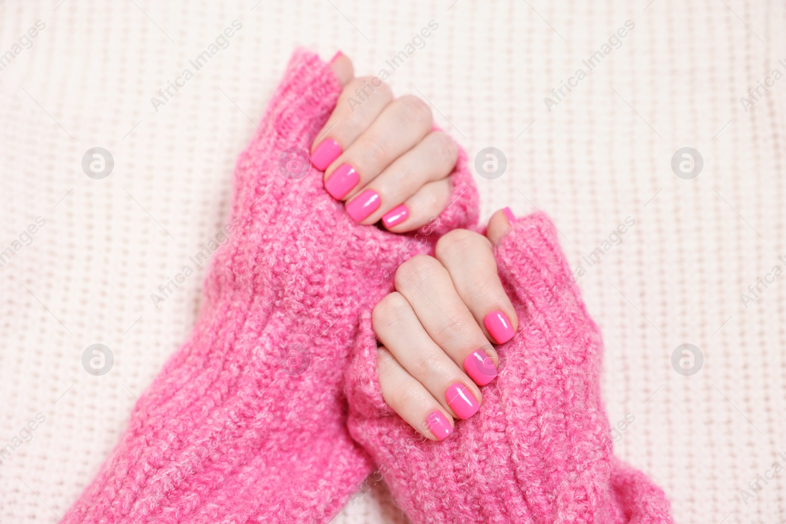 Photo of Woman showing her manicured hands with pink nail polish on knitted blanket, top view