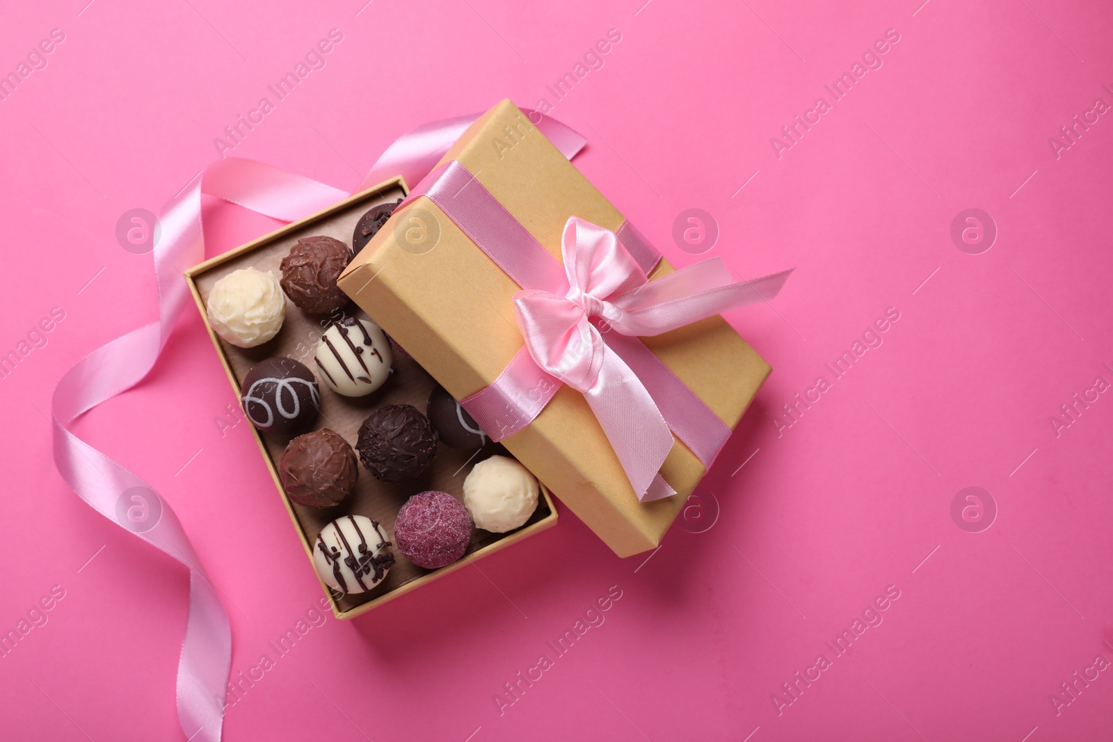 Photo of Open box with delicious chocolate candies and ribbon on pink background, top view. Space for text