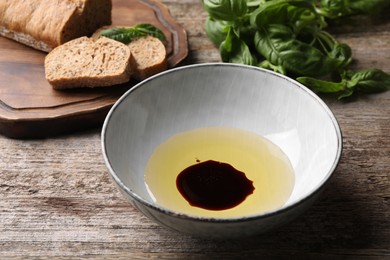Photo of Bowl of balsamic vinegar with oil and bread on old wooden table, closeup