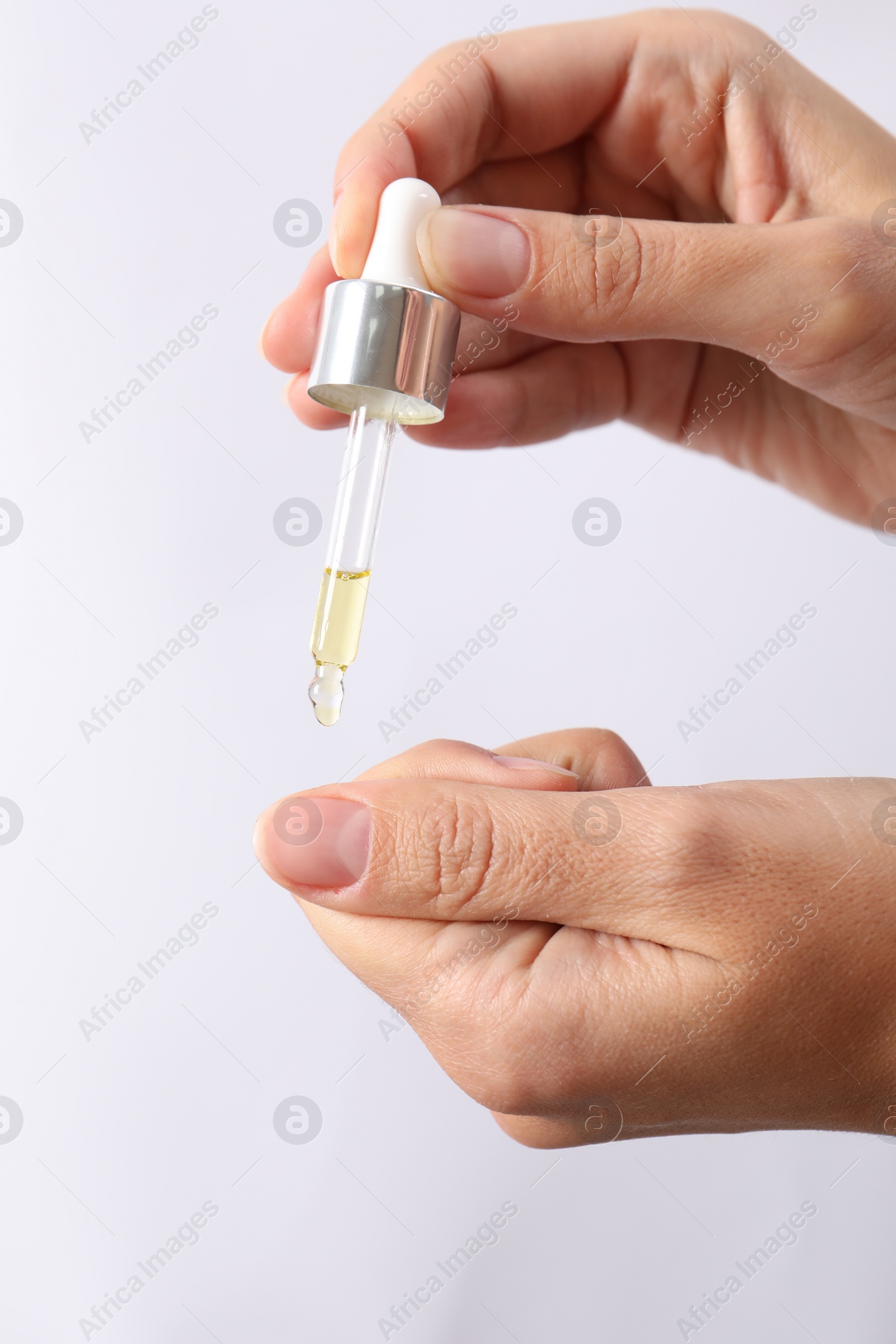 Photo of Woman applying cosmetic serum onto her finger on white background, closeup