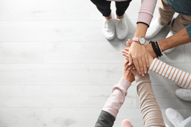 Photo of People holding hands together over light wooden background, top view with space for text. Unity concept