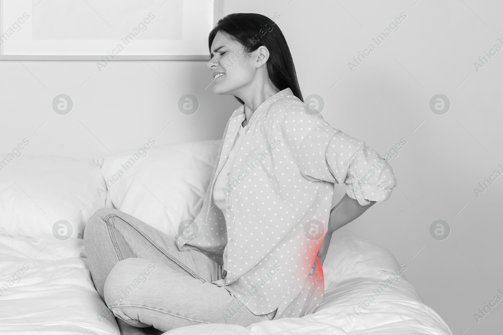 Image of Woman suffering from back pain indoors. Black and white effect with red accent