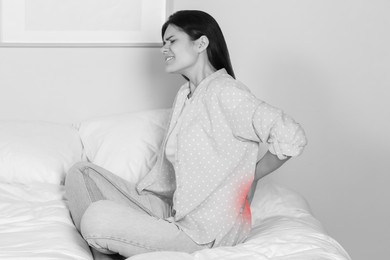 Image of Woman suffering from back pain indoors. Black and white effect with red accent