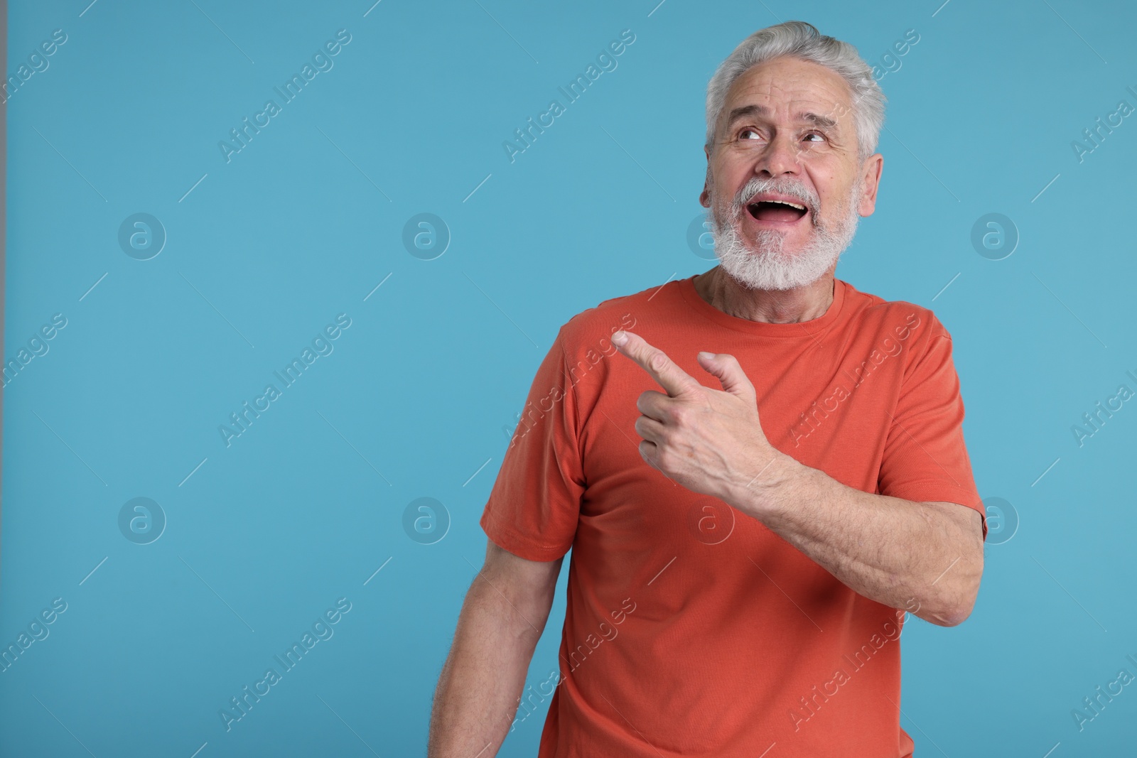 Photo of Surprised senior man pointing at something on light blue background, space for text