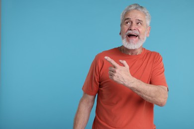 Photo of Surprised senior man pointing at something on light blue background, space for text