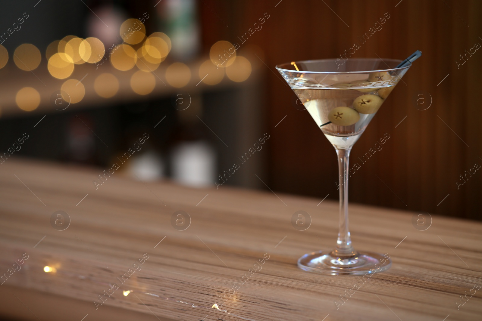 Photo of Delicious martini cocktail with olives on table in bar, space for text