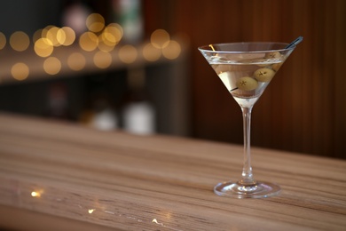 Photo of Delicious martini cocktail with olives on table in bar, space for text