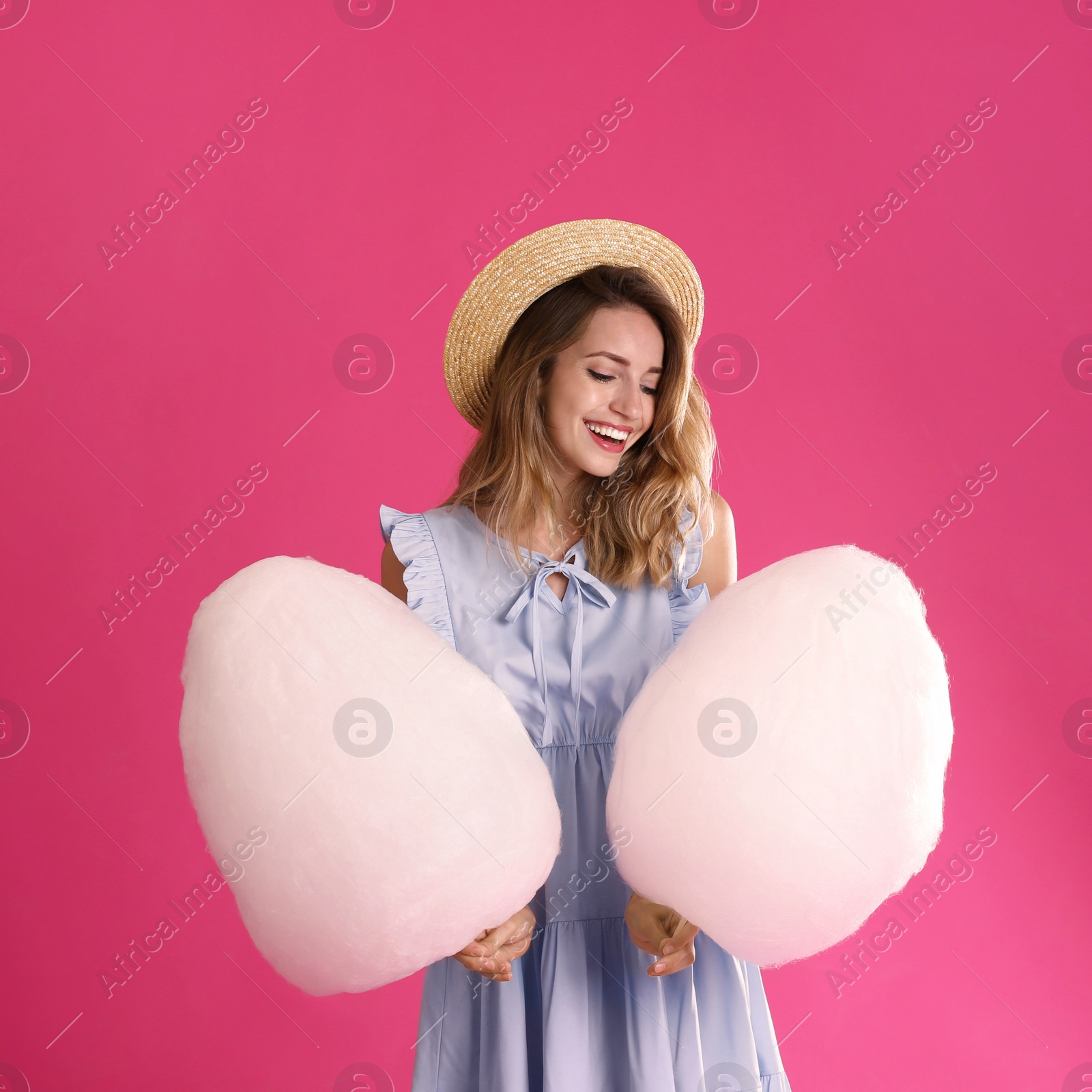 Photo of Happy young woman with cotton candies on pink background