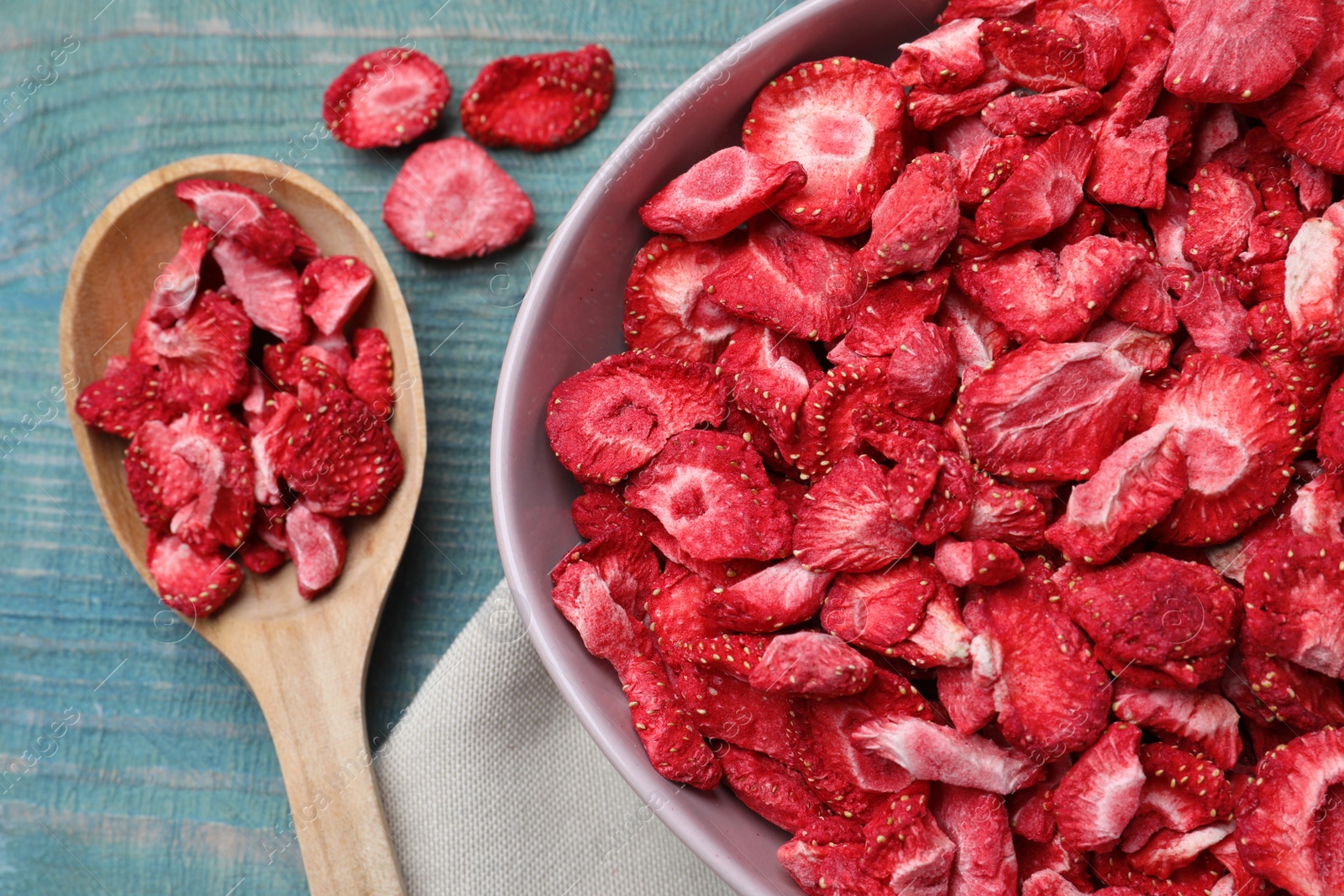 Photo of Bowl and spoon with dried strawberries on light blue wooden table, flat lay