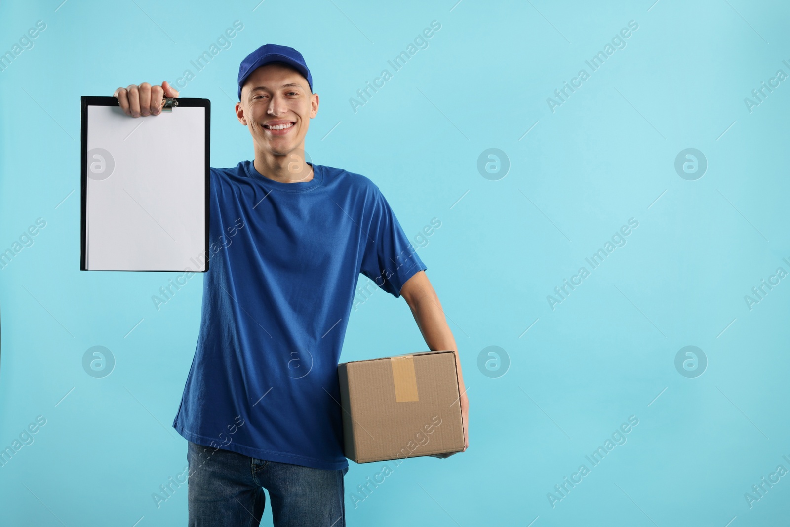 Photo of Happy courier with parcel and clipboard on light blue background. Space for text