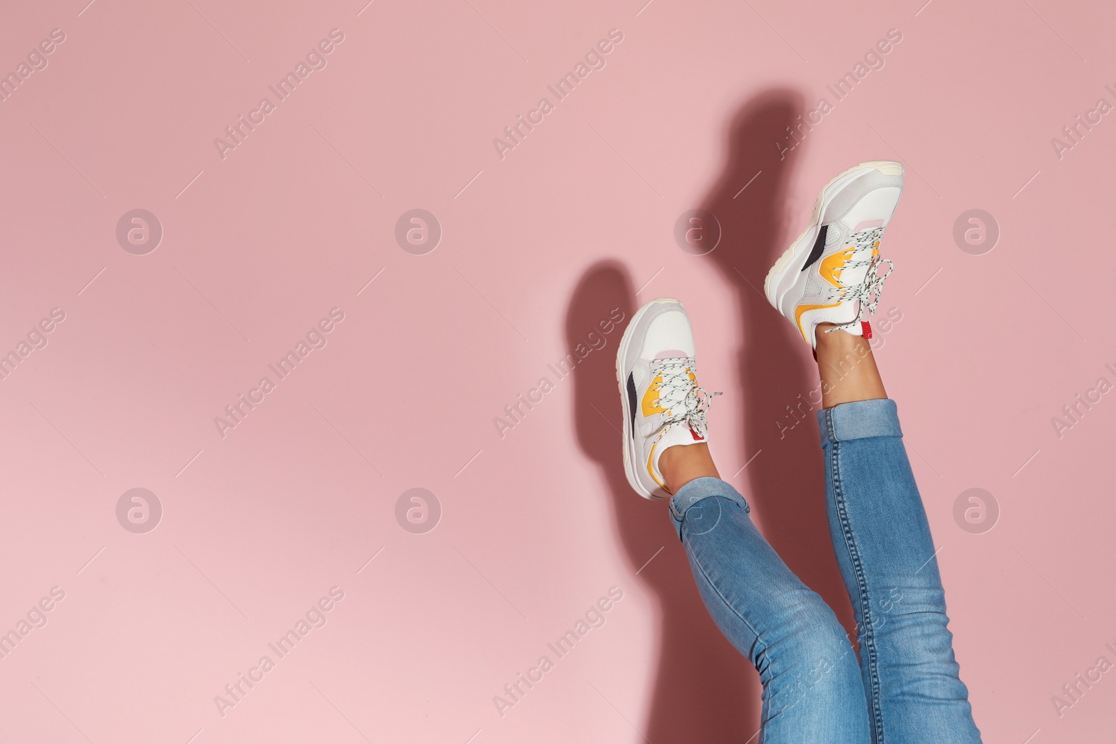 Photo of Woman in stylish sneakers near color wall, closeup. Space for text