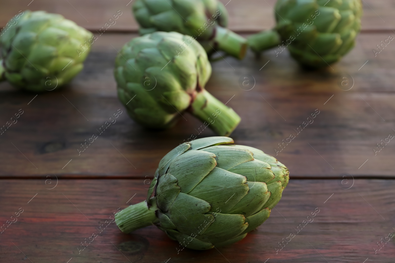 Photo of Whole fresh raw artichokes on wooden table, closeup