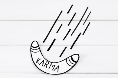 Paper boomerang with word Karma on white wooden table, flat lay