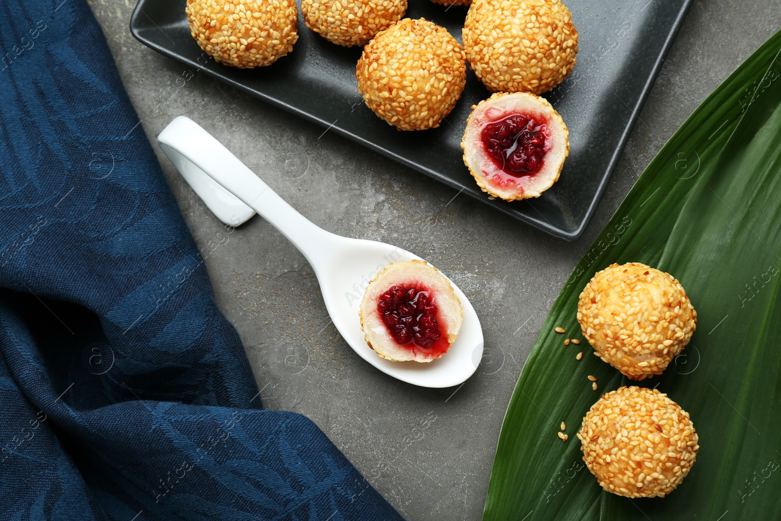 Photo of Delicious sesame balls, spoon and green banana leaf on grey table, flat lay