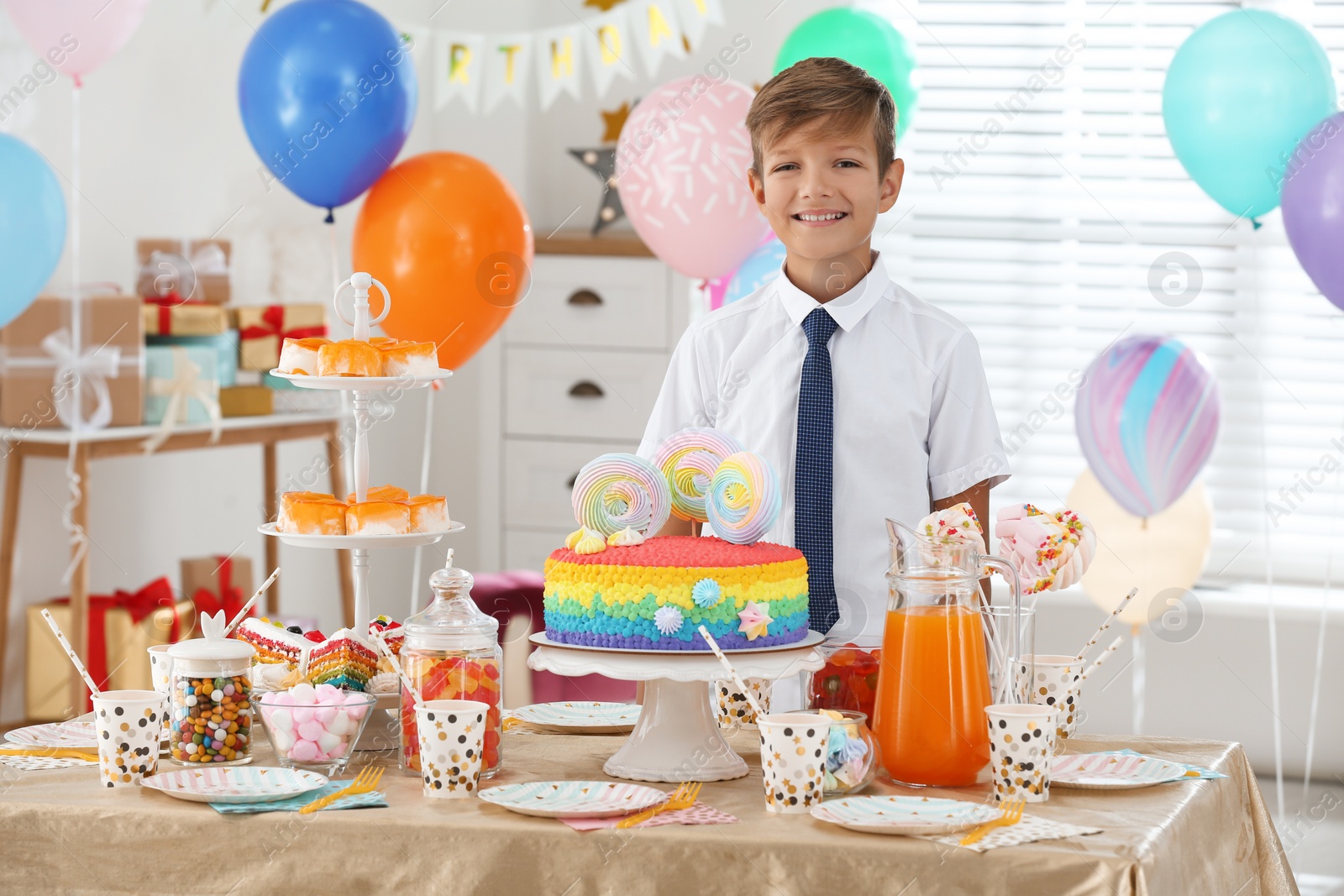 Photo of Happy boy at table with treats in room decorated for birthday party