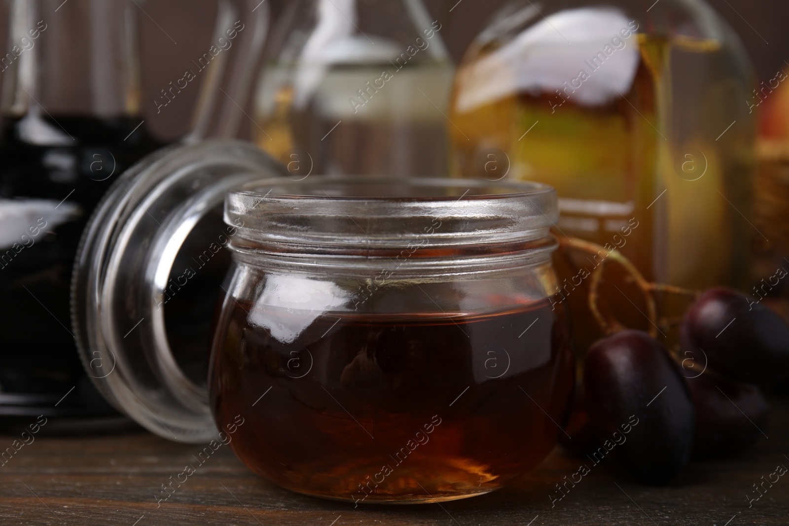 Photo of Different types of vinegar and grapes on wooden table, closeup