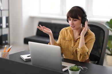 Photo of Woman in headphones watching webinar at table in office