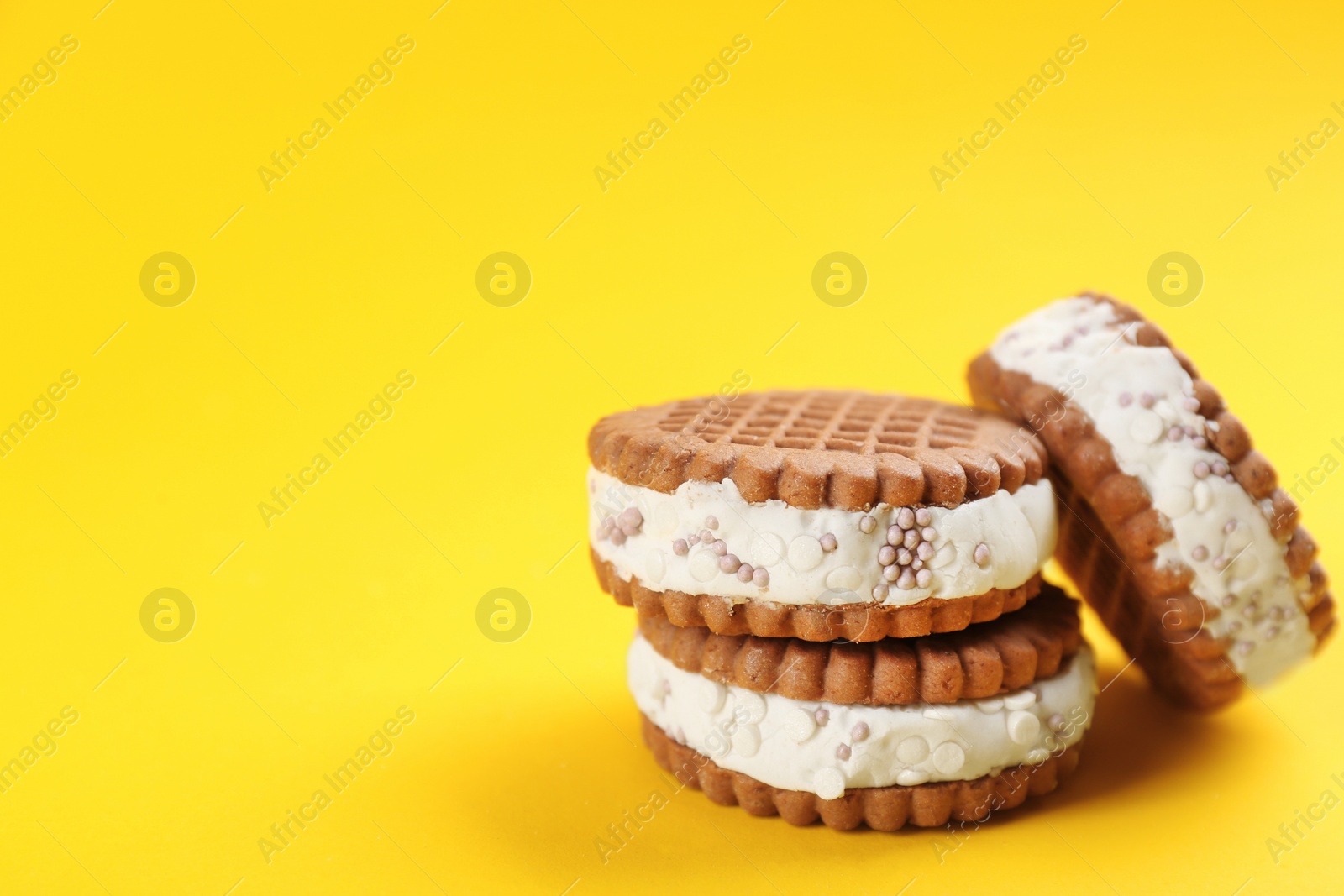 Photo of Sweet delicious ice cream cookie sandwiches on yellow background. Space for text