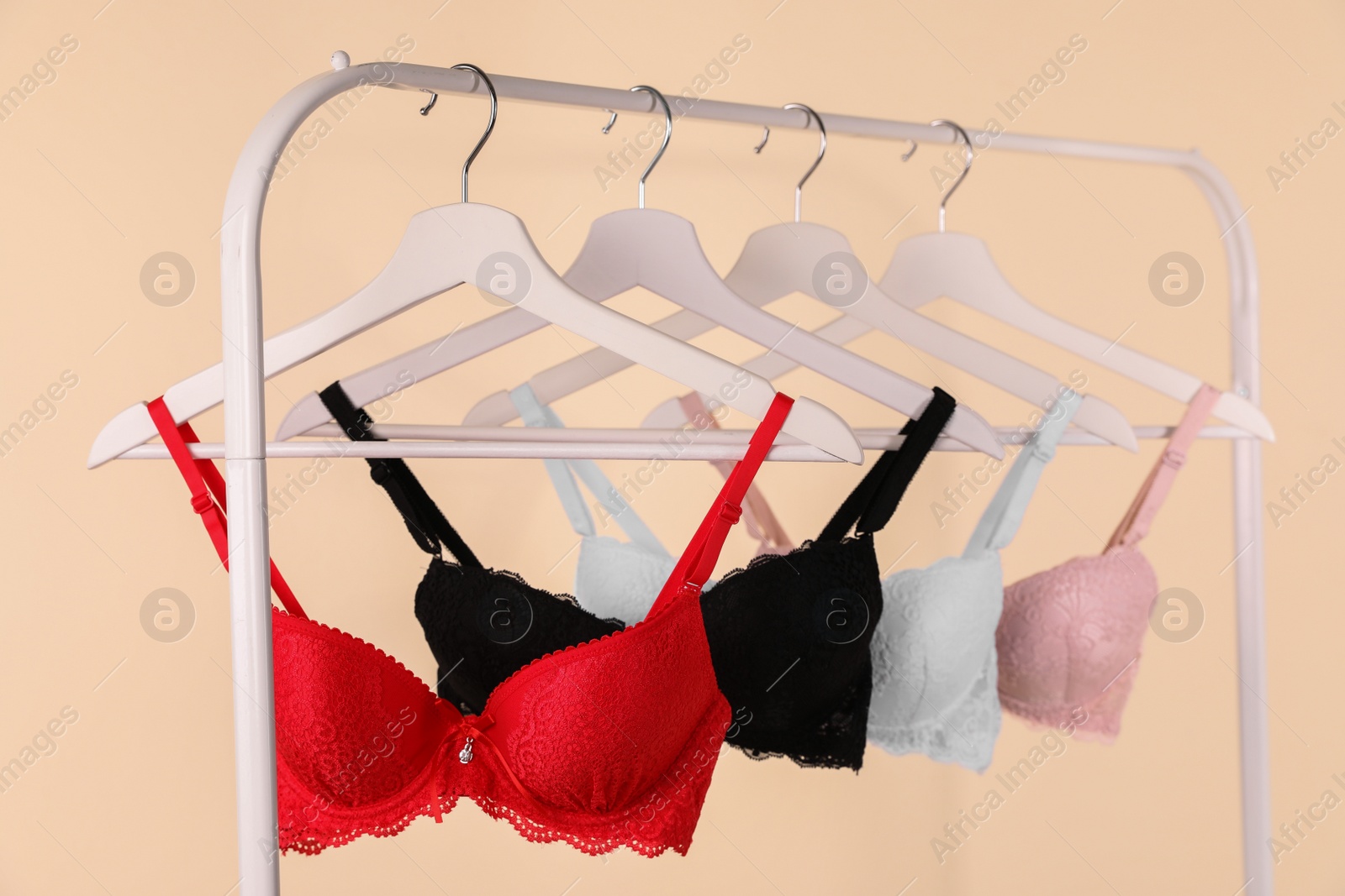 Photo of Hangers with beautiful lace bras on rack against beige background. Stylish underwear