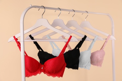 Hangers with beautiful lace bras on rack against beige background. Stylish underwear