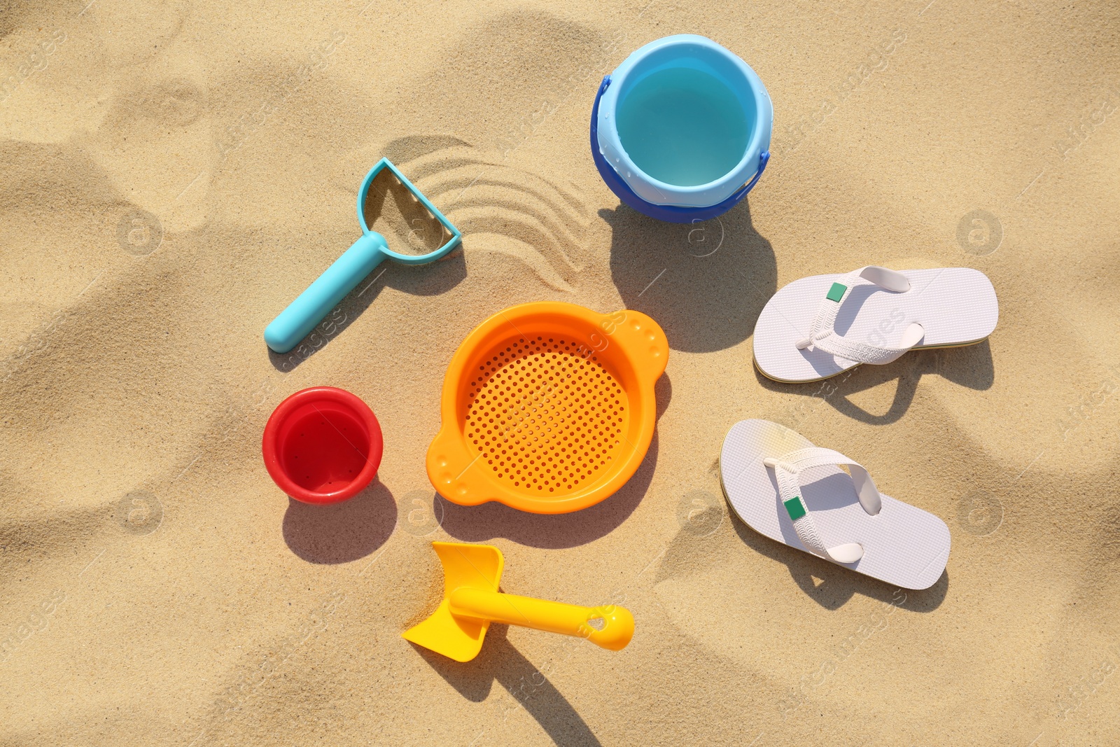 Photo of Set of plastic beach toys and flip flops on sand, flat lay. Outdoor play