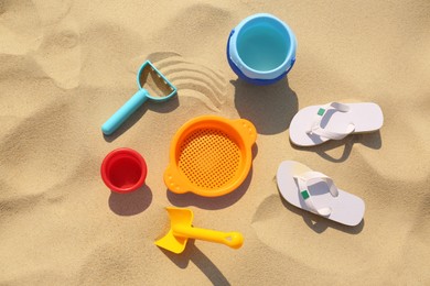 Photo of Set of plastic beach toys and flip flops on sand, flat lay. Outdoor play