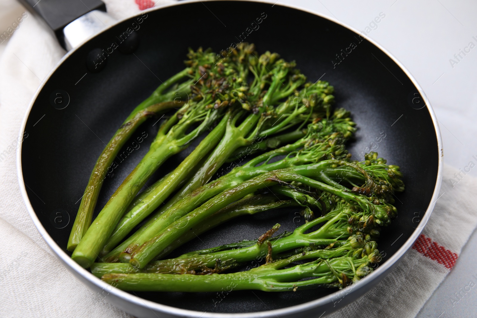 Photo of Frying pan with tasty cooked broccolini on table, closeup