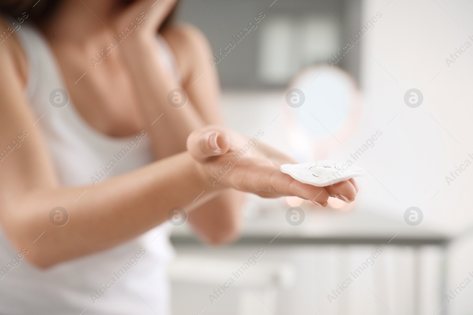 Photo of Young woman holding cotton pad with fallen eyelashes indoors