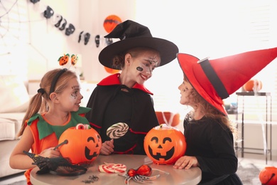 Photo of Cute little kids with pumpkin candy buckets wearing Halloween costumes at home