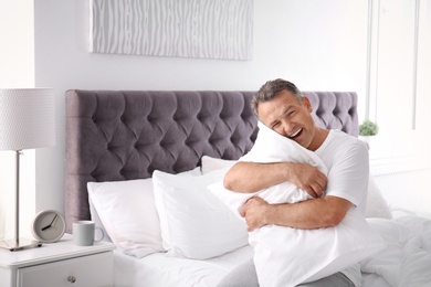 Photo of Happy man with soft pillow sitting on bed at home