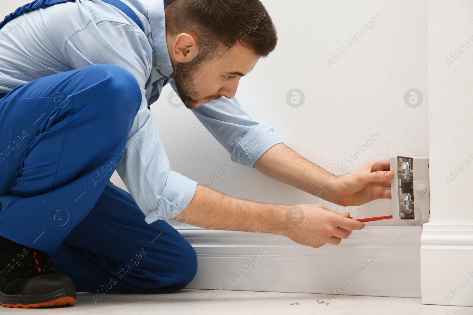 Photo of Electrician with screwdriver repairing power socket indoors