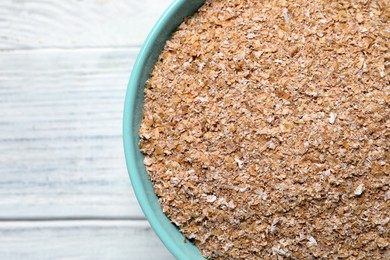 Photo of Bowl of wheat bran on white wooden table, top view