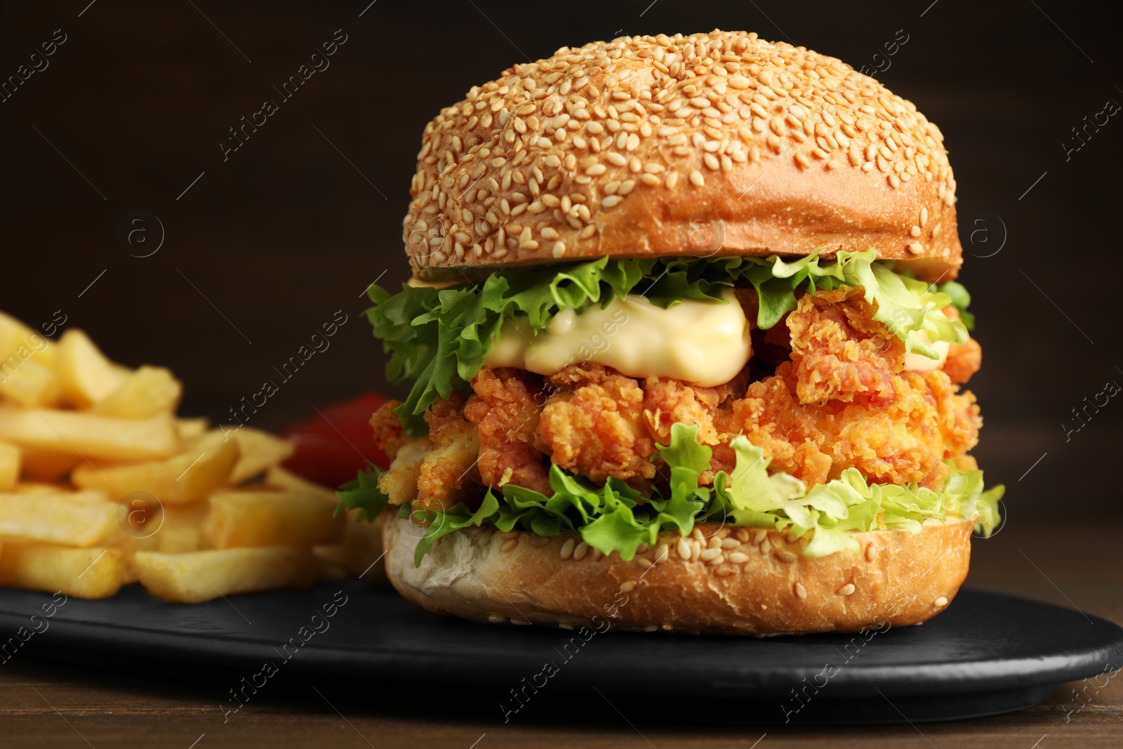 Photo of Delicious burger with crispy chicken patty and french fries on wooden table, closeup