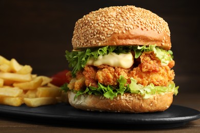 Photo of Delicious burger with crispy chicken patty and french fries on wooden table, closeup