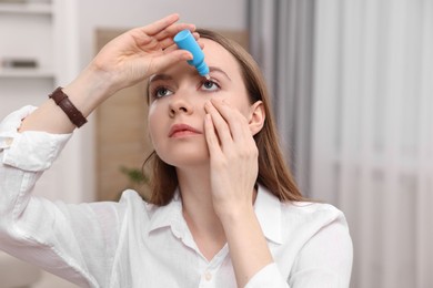 Photo of Young woman applying medical eye drops indoors