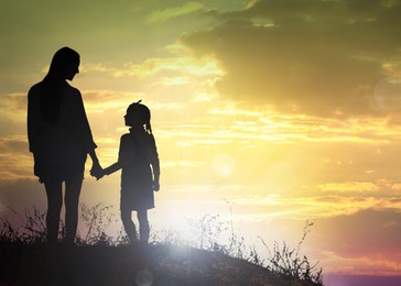 Silhouettes of godparent with child in field at sunset, space for text