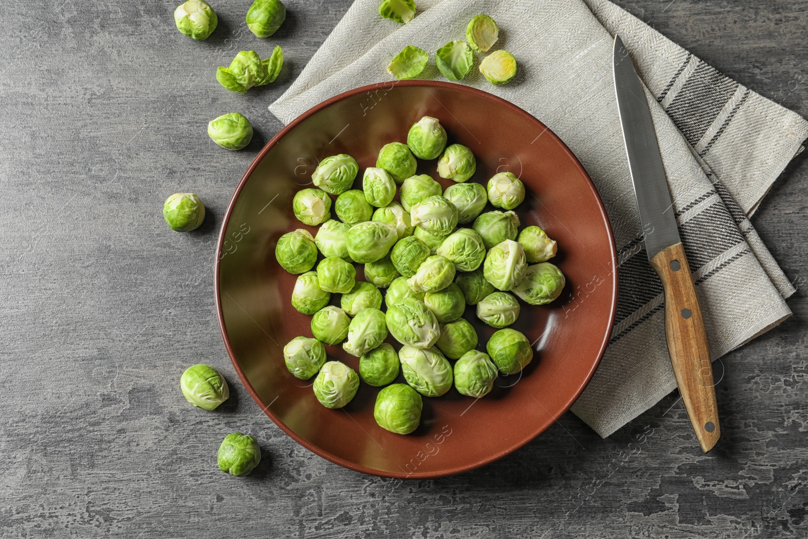 Photo of Plate of fresh Brussels sprouts, napkin and knife on grey background, top view