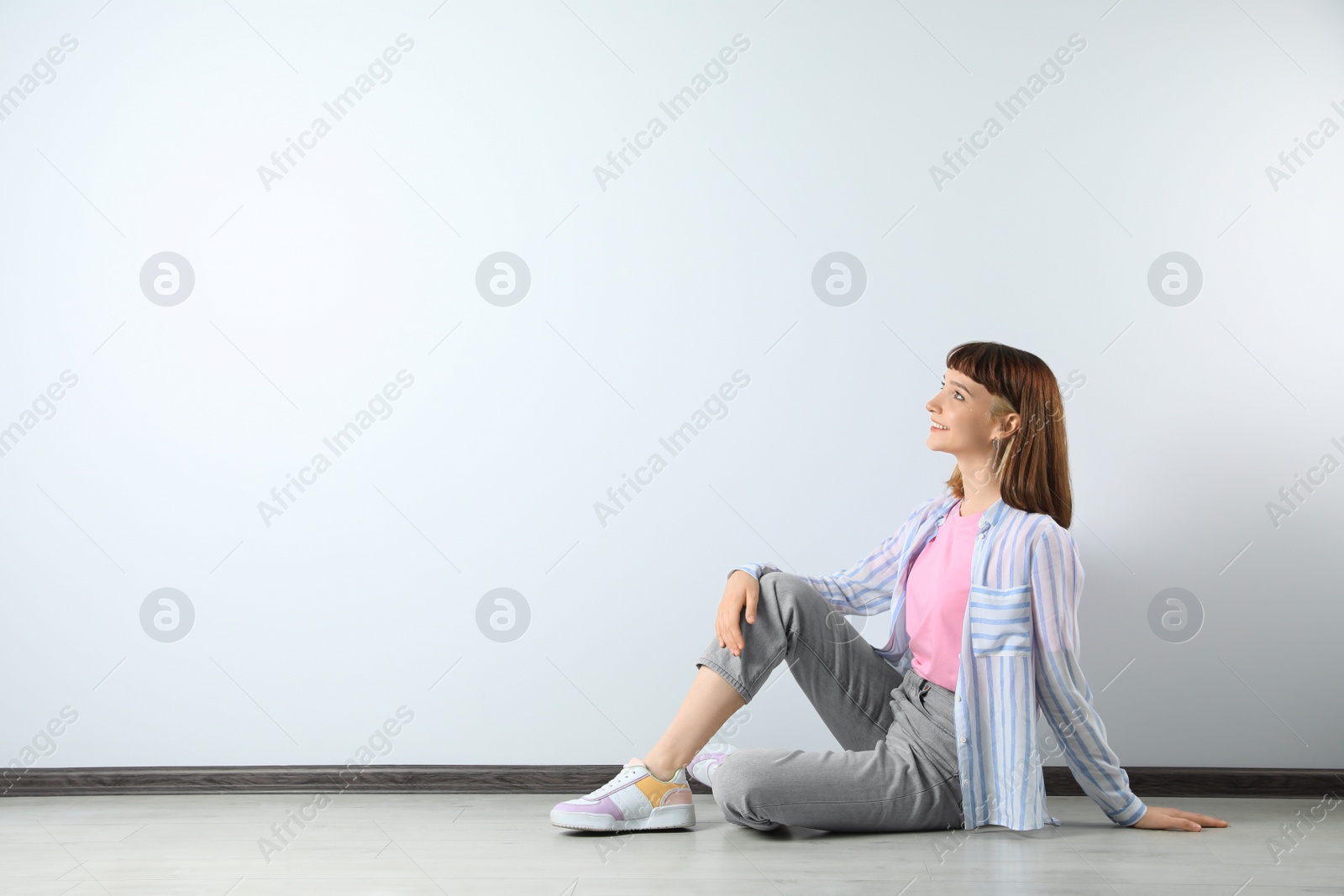 Photo of Beautiful young girl sitting on floor near white wall. Space for text