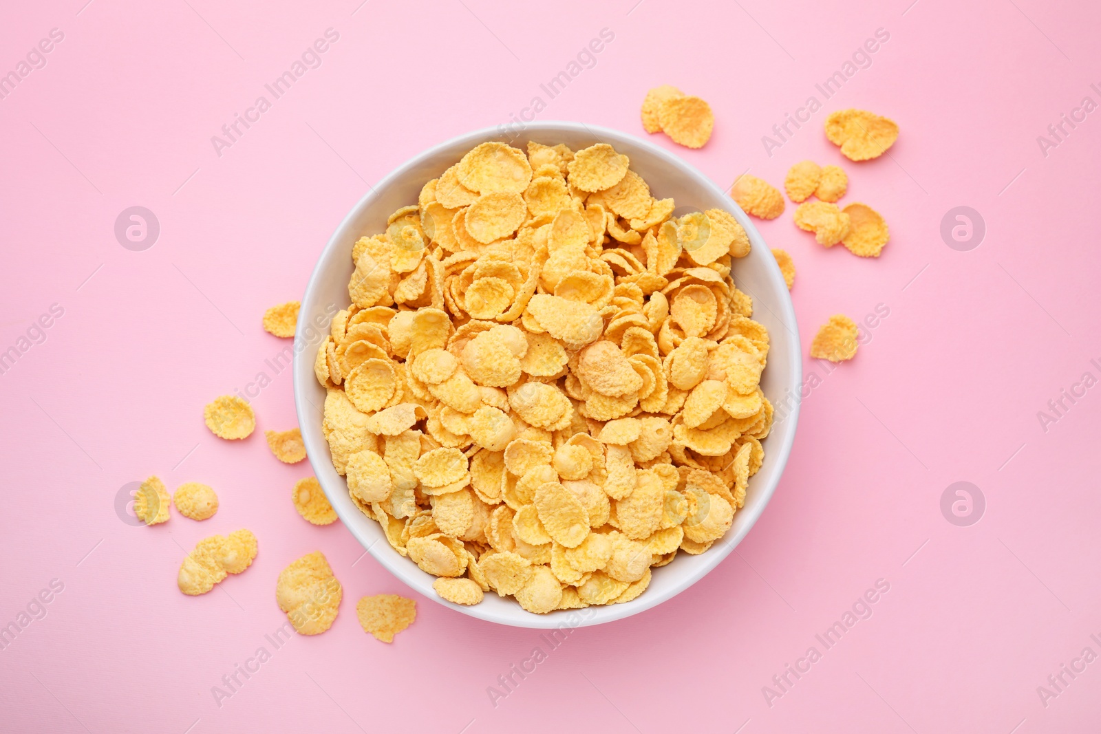 Photo of Breakfast cereal. Tasty corn flakes in bowl on pink table, top view