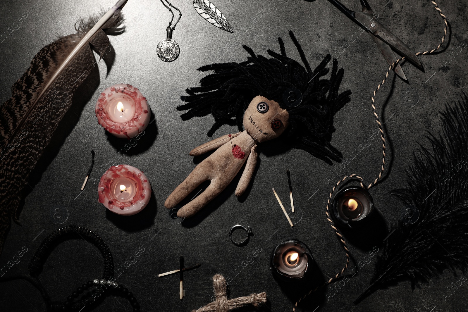 Photo of Female voodoo doll with pin in heart and ceremonial items on grey table, flat lay